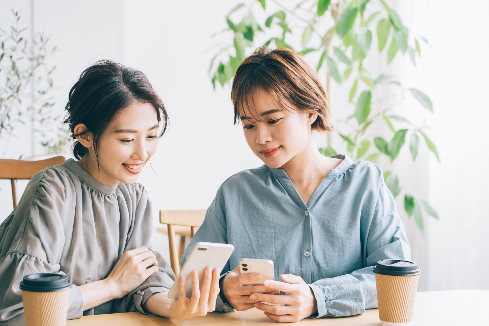 カフェでスマホを見る笑顔の女性2人組