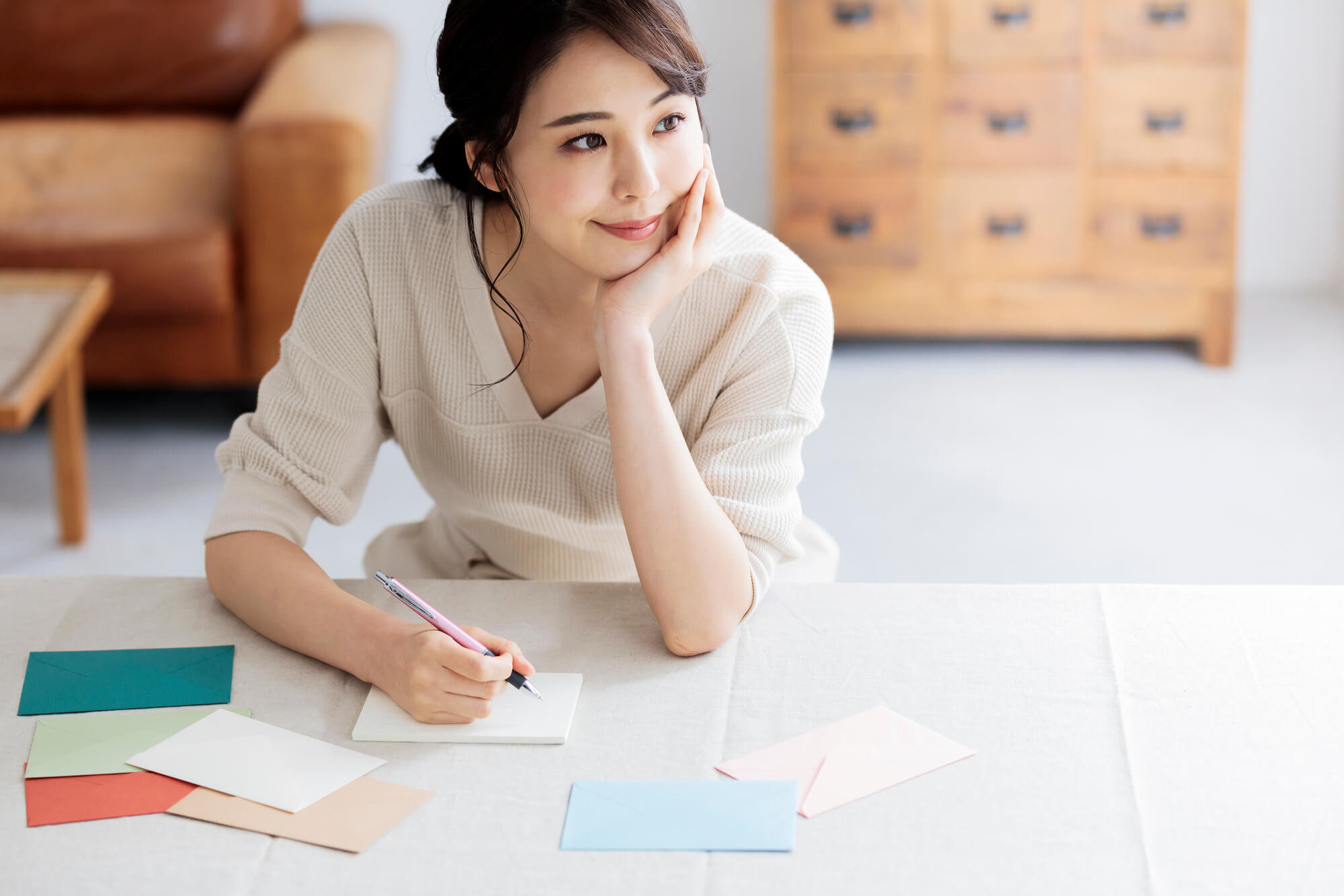窓辺で手紙を書く若い女性 顔に手を置き考えているシーン