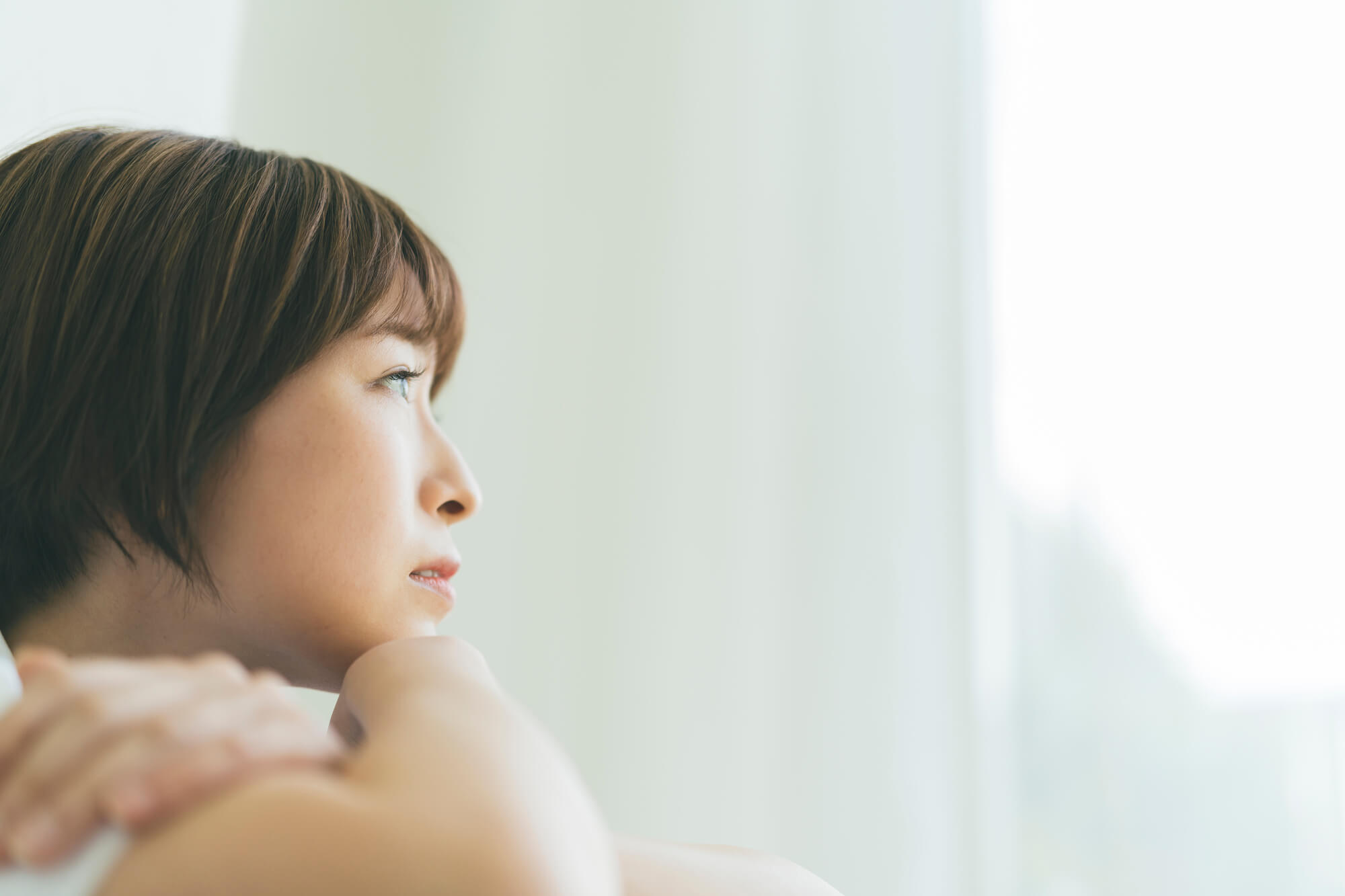 腕をくみ外を眺めながら悩む女性